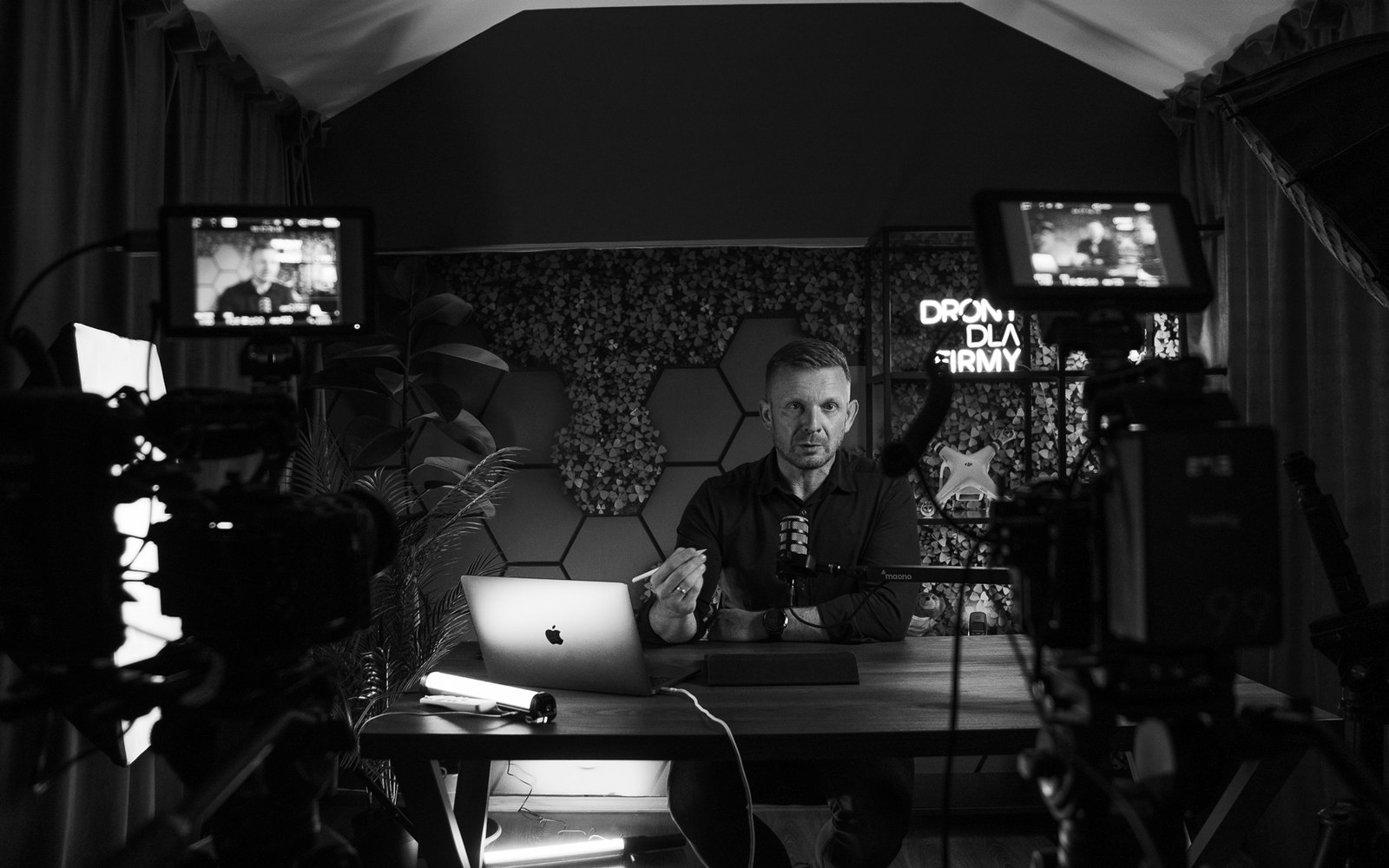 Gotowe studio Drony dla Firmy: prowadzący przy stole, dwie kamery z podglądem, softbox, ściana z heksagonami i neon marki